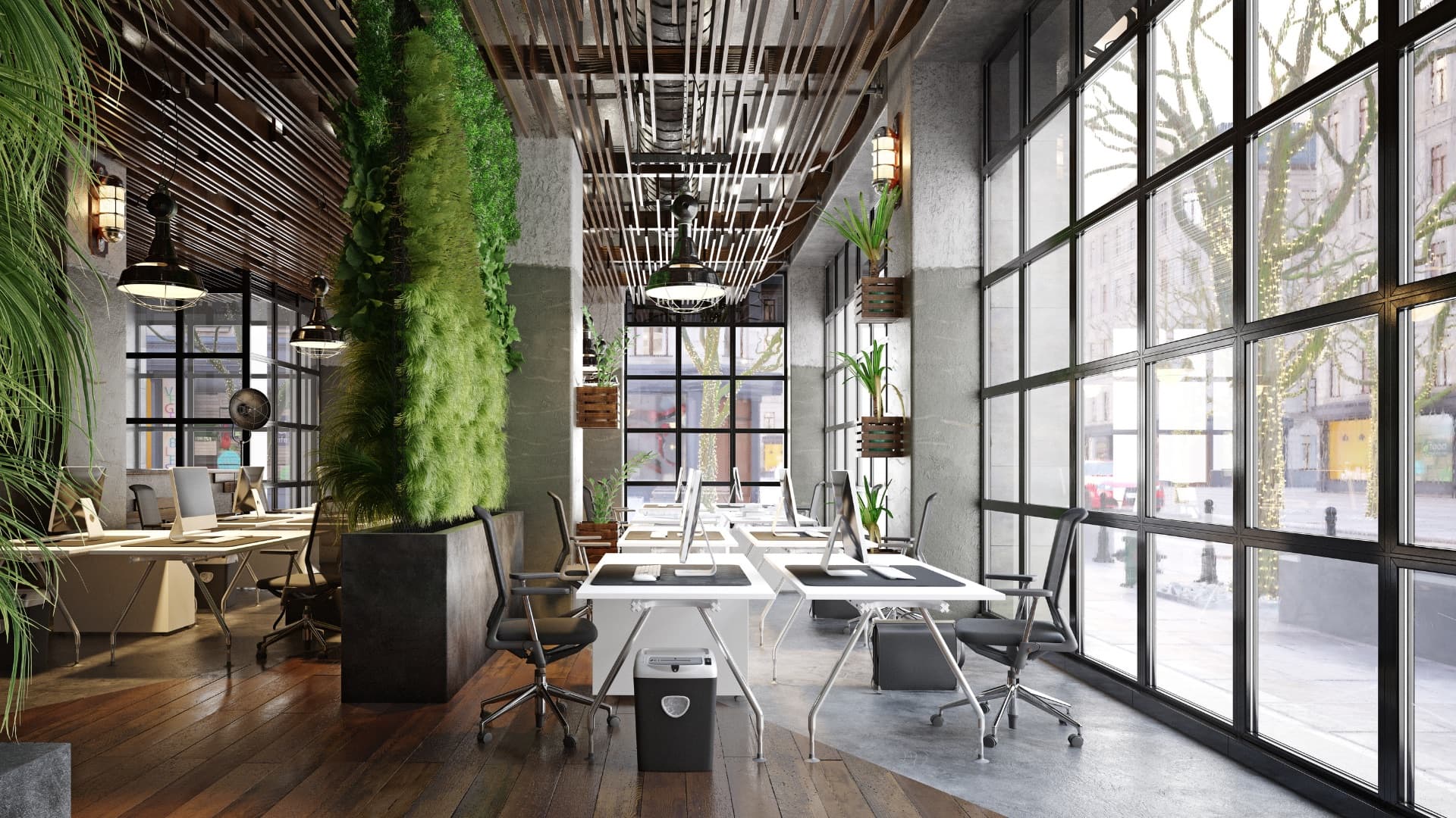 A plant-lined office of white desks in front of full-height windows